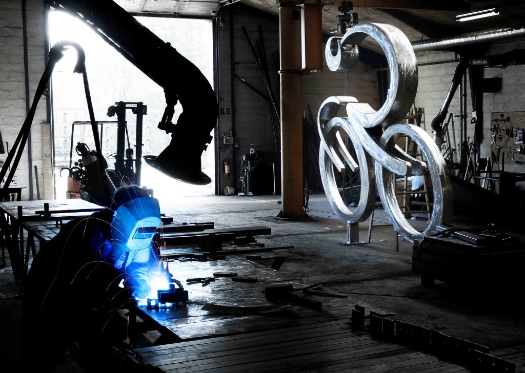 Billede af cykkel skulptur i værkstedet, med smed i forgrunden.